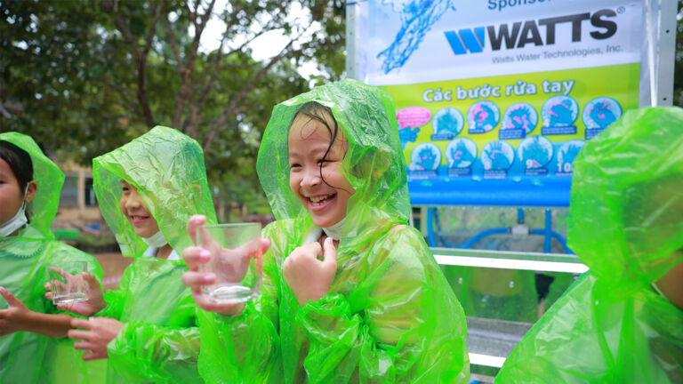 Girls drinking water with green poncho rain coverings on.